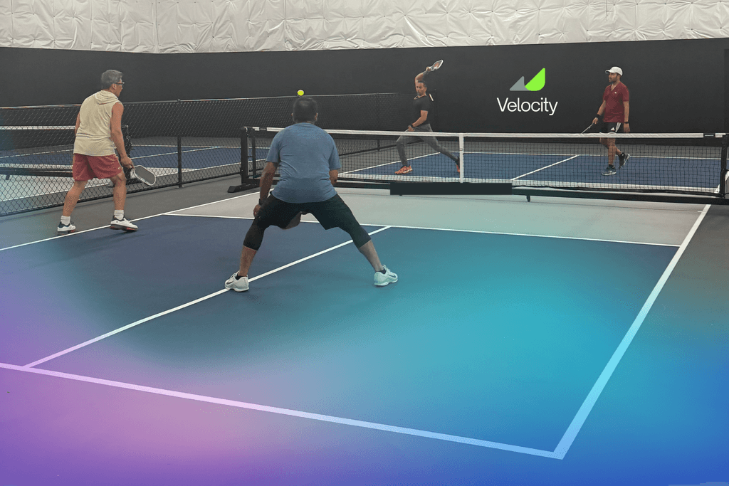 Players rallying on blue indoor pickleball courts at Velocity Pickleball Club